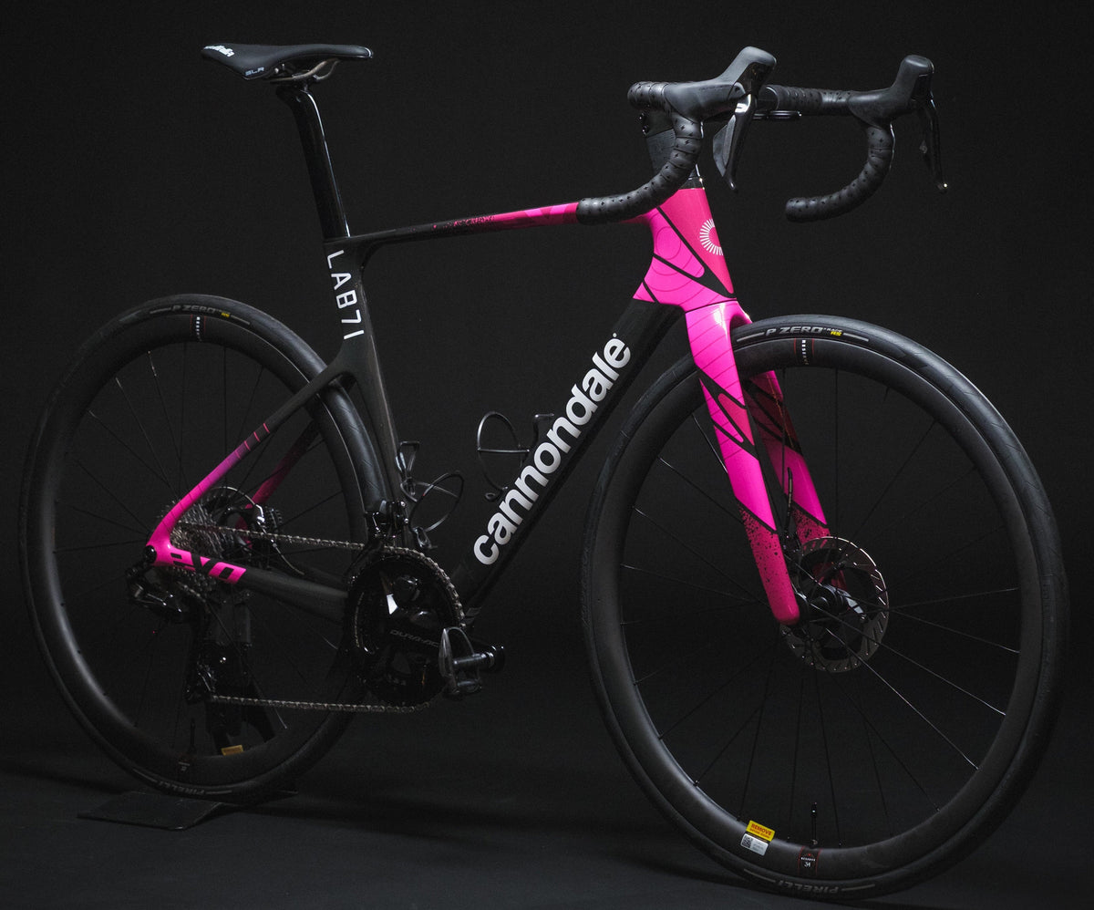 A Cannondale road bicycle with a black frame and bright pink geometric graphics, photographed on a dark studio background.